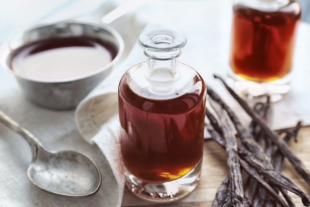 Das Bild zeigt zwei Flaschen mit flüssigem Aromaextrakt sowie mehreren getrockneten Vanilleschoten auf einem Tisch